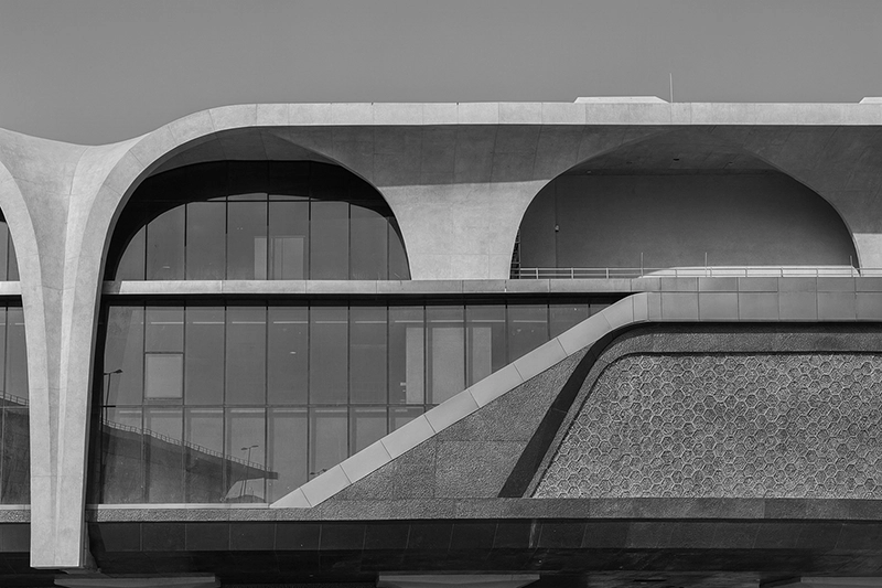 Modern building facade with large glass windows and curved, concrete architectural elements in black and white. Red Line South Metro Doha, Al Wakra Station.