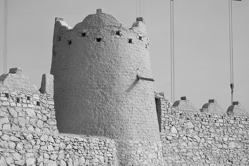 Historic stone fortress wall with a large central round tower featuring small square openings near the top. Diriyah, Riyadh, KSA.