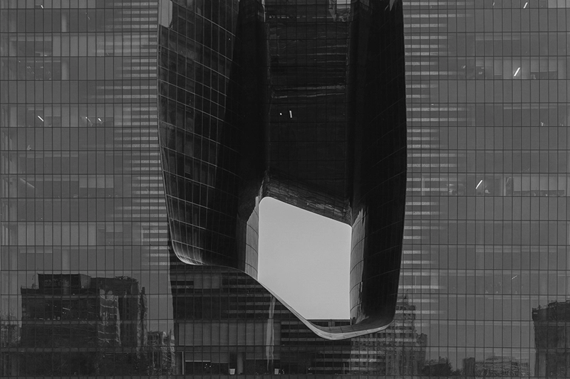 Close-up of a modern glass skyscraper with a large curved rectangular cutout in the center reflecting nearby buildings. Opus Pentouse, Dubai, UAE.