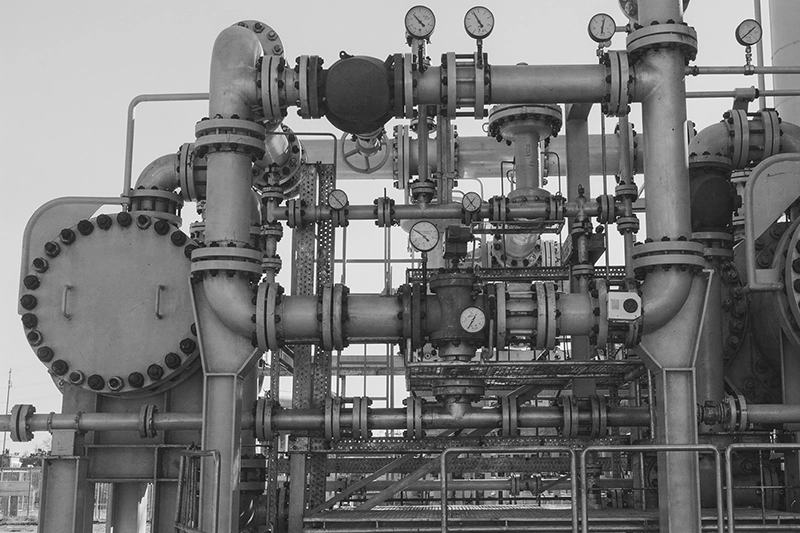 Complex network of industrial metal pipes and valves with pressure gauges in an outdoor setting.